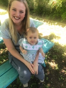 Blond woman with baby in her lap, sitting on a bench smiling