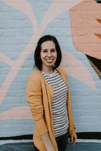 White woman with brown hair smiles in front of a colorful wall